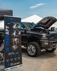 A Hydra Thrive IV therapy banner beside a lifted pickup truck at an outdoor show