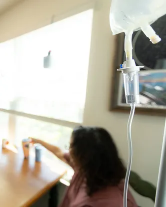 An IV bag and drip line hanging in a client’s kitchen, with the client seated at the table behind it