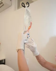 Gloved hands preparing an IV bag on a stand