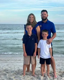Meghan with her husband and two sons on a beach at sunset